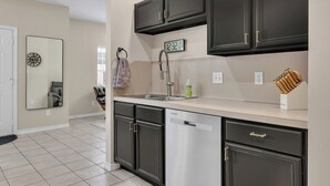 A kitchen with dark cabinets, a stainless steel dishwasher, a clock, and a knife block. - TikTok: Walk to Texas A&M Campus, Sleep 8, 3BR/3BA (College Station)