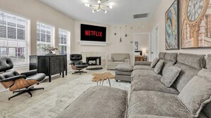 A modern living room with a large gray sectional sofa, a black leather chair, a wooden coffee table, and a fireplace. - TikTok: Walk to Texas A&M Campus, Sleep 8, 3BR/3BA (College Station)