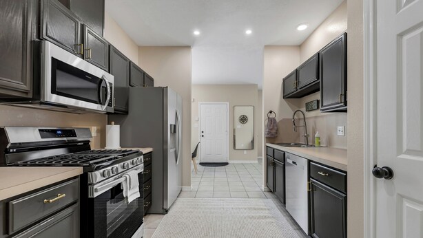 A modern kitchen with stainless steel appliances, dark cabinetry, and a tiled floor. - TikTok: Walk to Texas A&M Campus, Sleep 8, 3BR/3BA (College Station)