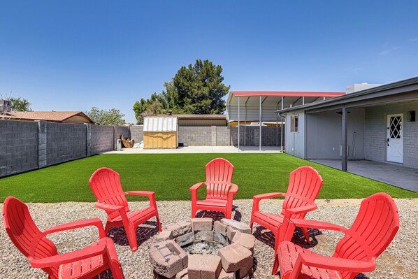 A backyard with a fire pit, red Adirondack chairs, and a covered patio area.