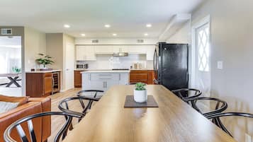 Une cuisine moderne avec des meubles blancs, un réfrigérateur noir et un coin repas comprenant une table et des chaises en bois.