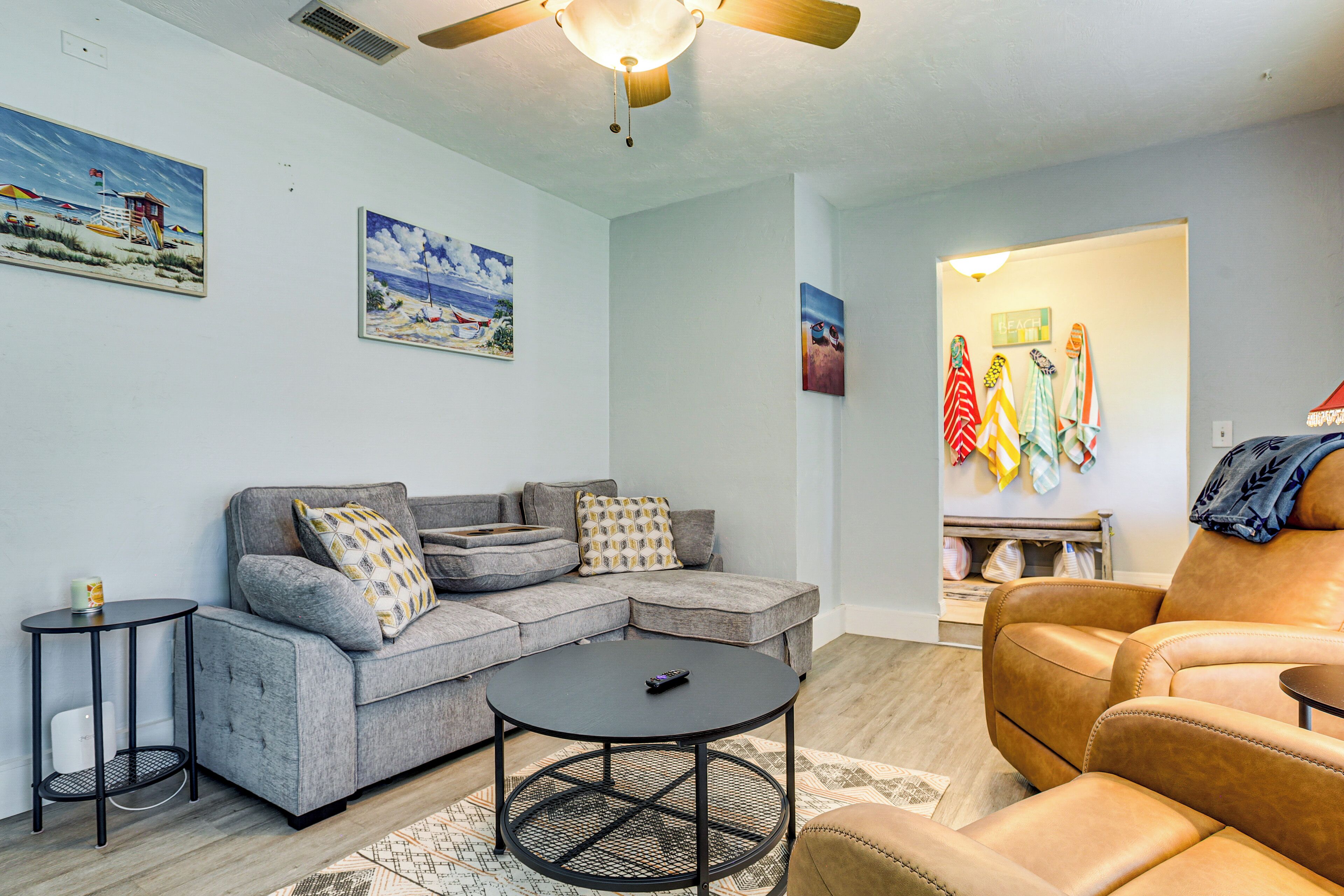 A living room with a sectional sofa, a round coffee table, a tan leather armchair, and a ceiling fan.