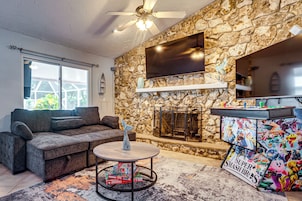 Una sala de estar con pared de piedra, un televisor de pantalla plana, chimenea, sofá y una mesa con juegos de mesa.