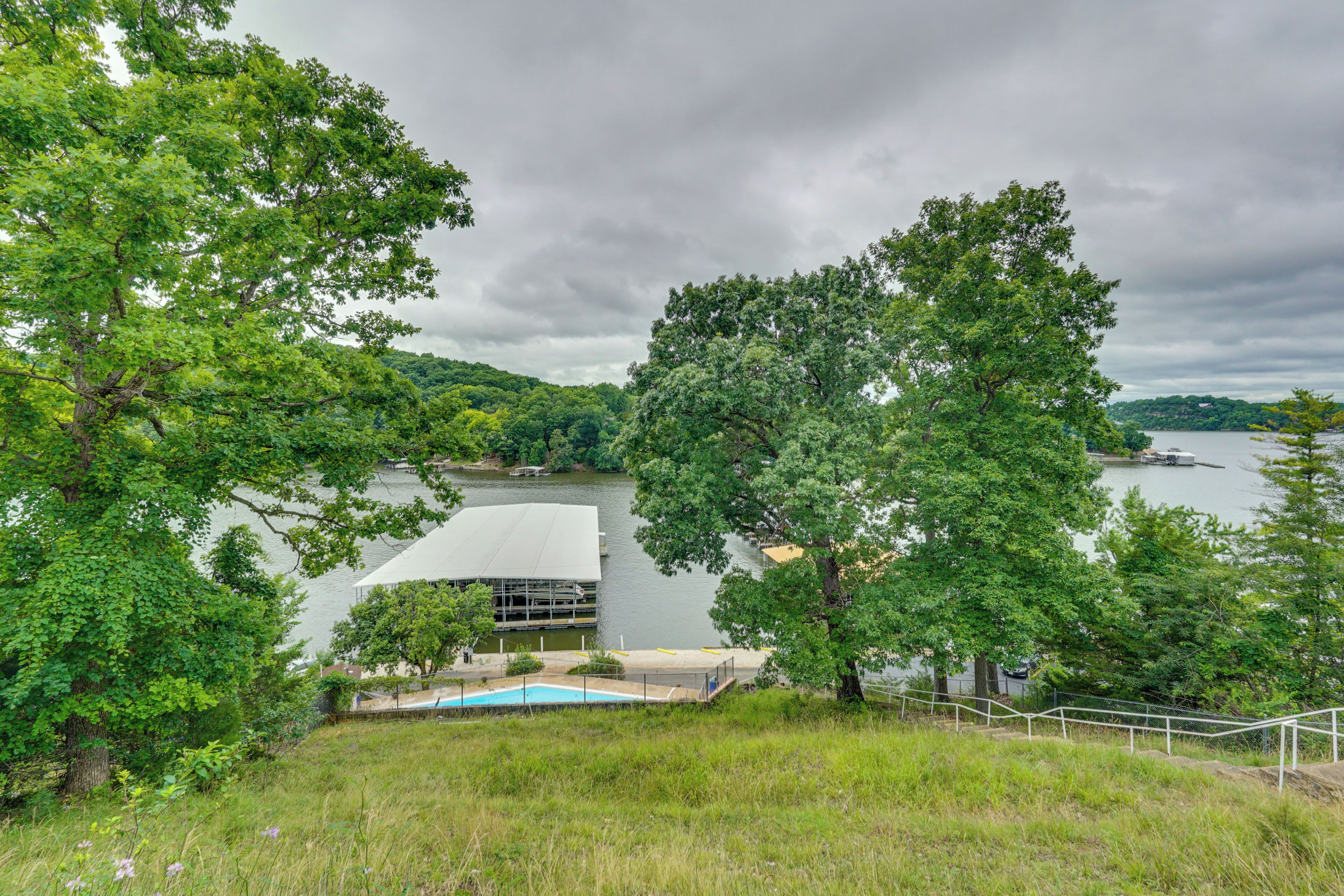 A lakeside view with a modern building, a swimming pool, and lush greenery.