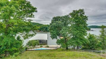 A lakeside view with a modern building, a swimming pool, and lush greenery.