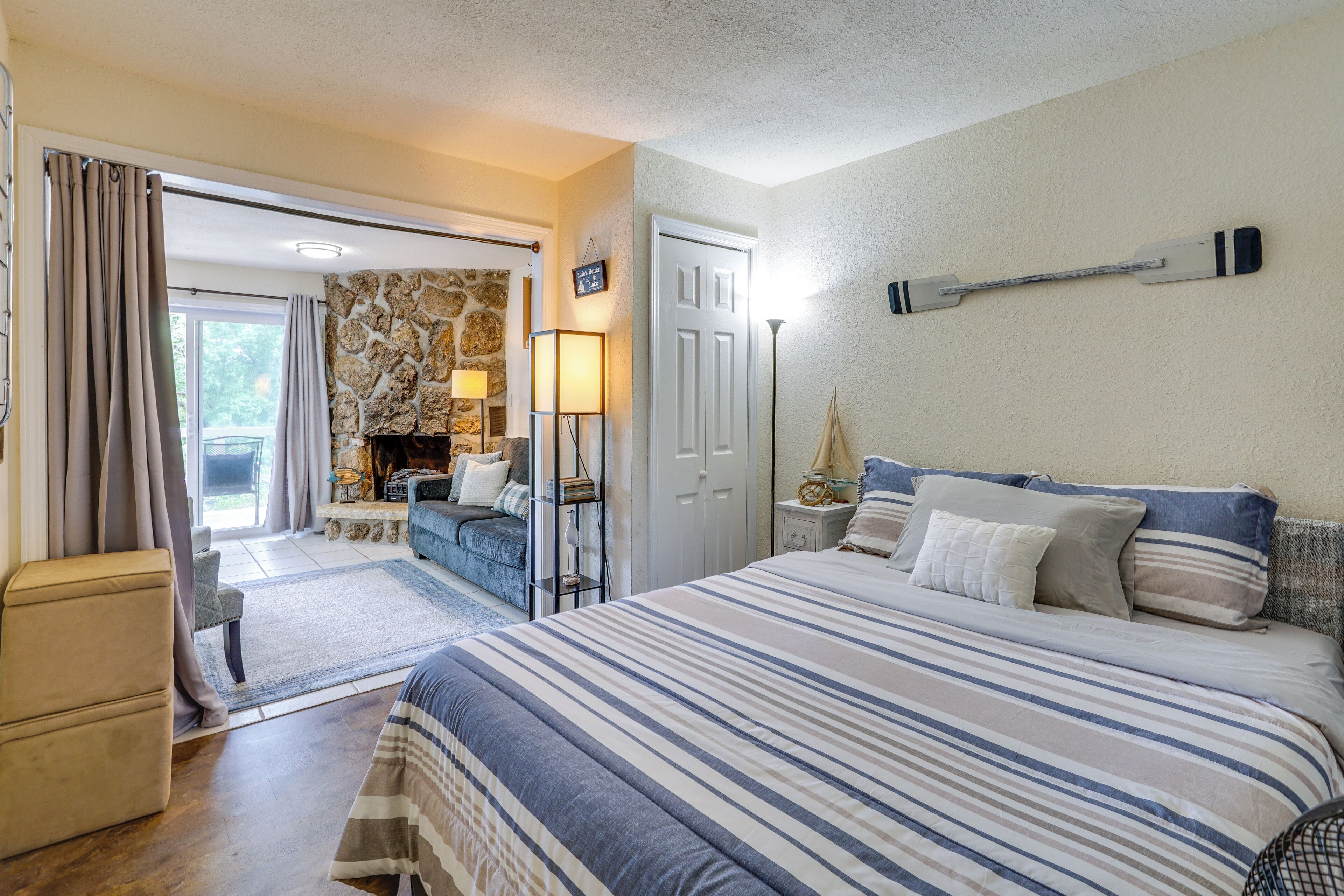 A bedroom with a large bed, a stone fireplace, a sofa, and a view of the outdoors.