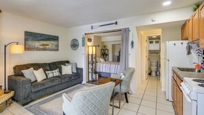 Un espacio habitable compacto con sofá, sillón, mesa de comedor, kitchenette y baño a la vista.