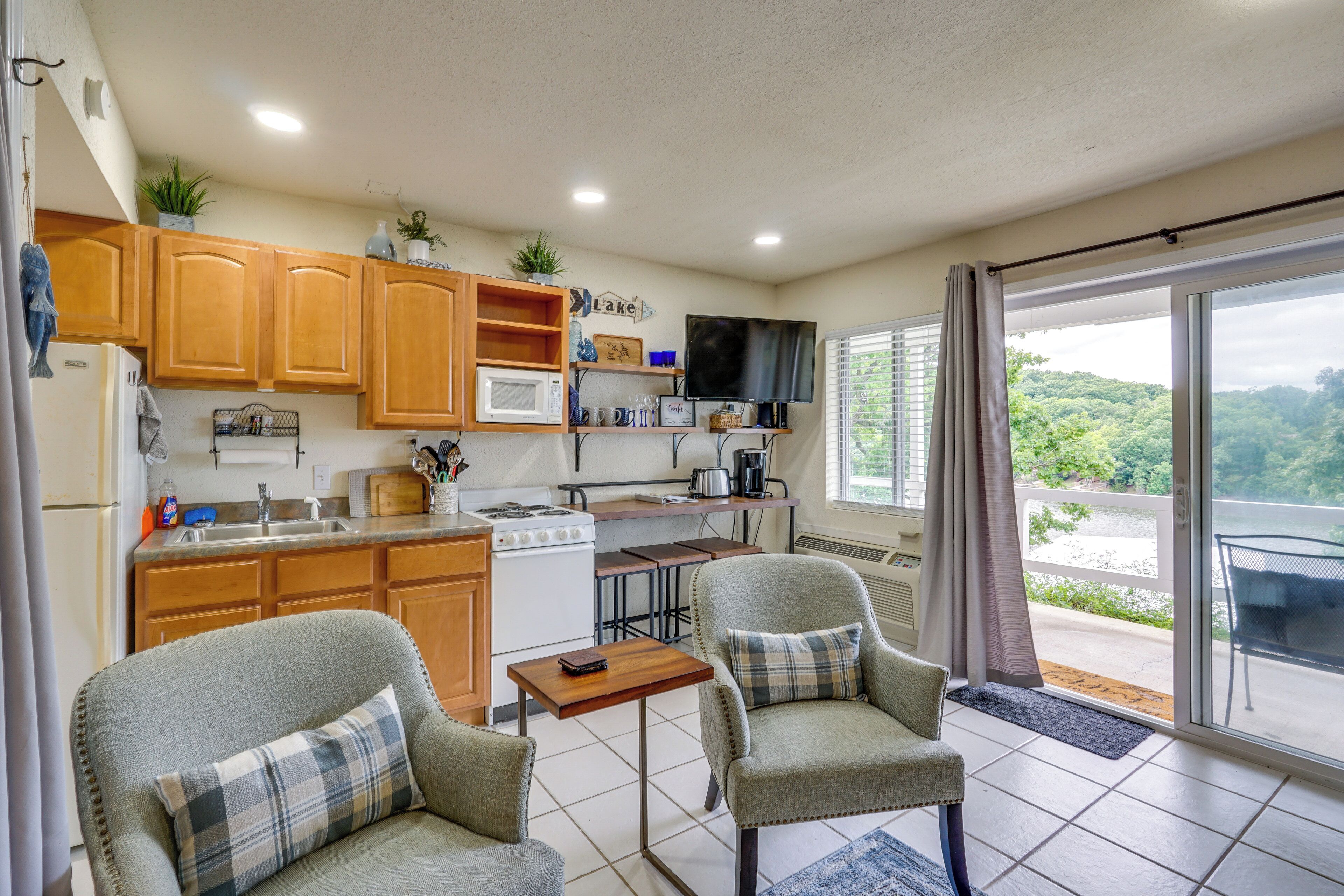 A compact kitchen with wooden cabinets, a microwave, a stove, and a dining area with two chairs.