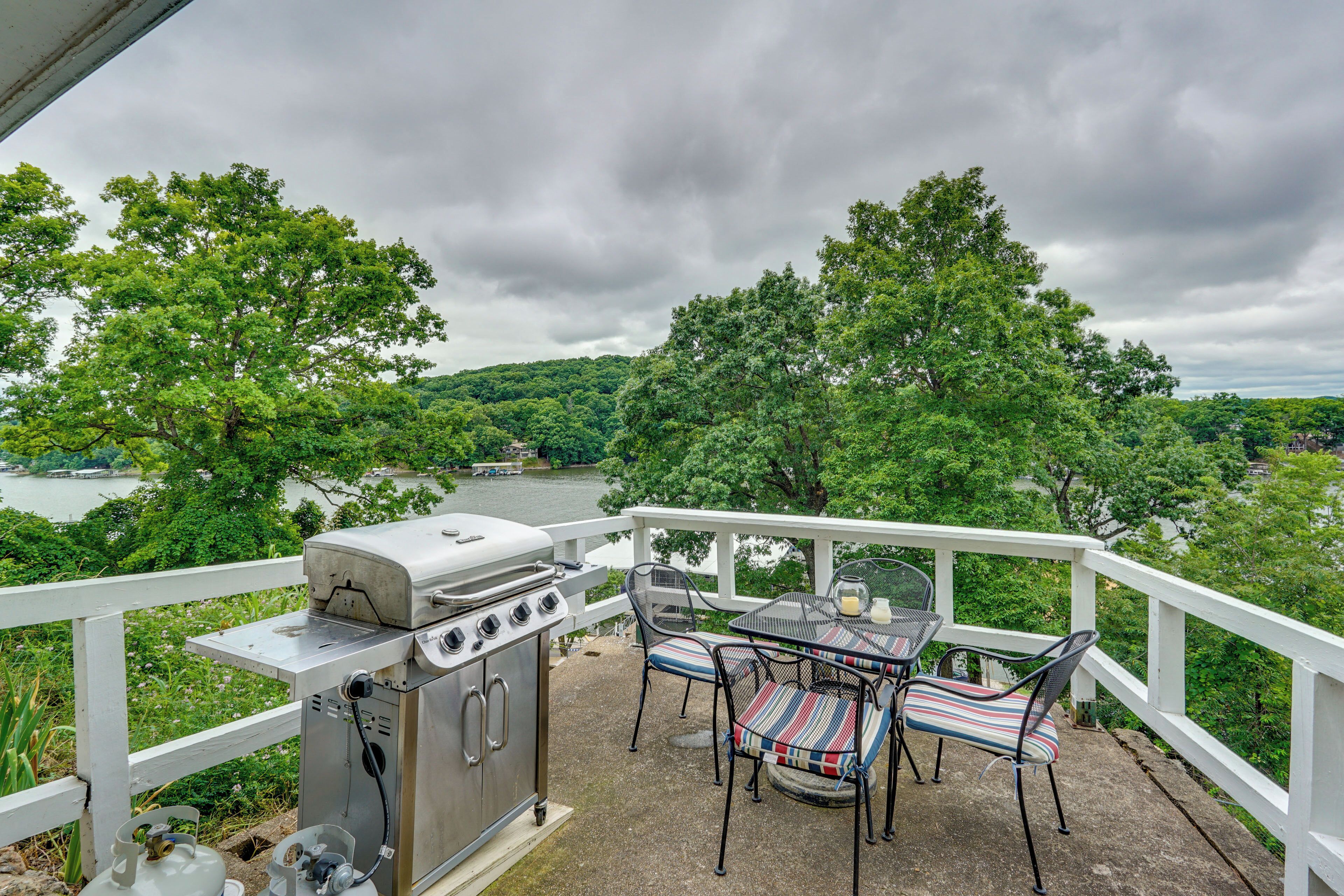 Un patio exterior con una parrilla, sillas y una mesa, con vistas a un río y un bosque.