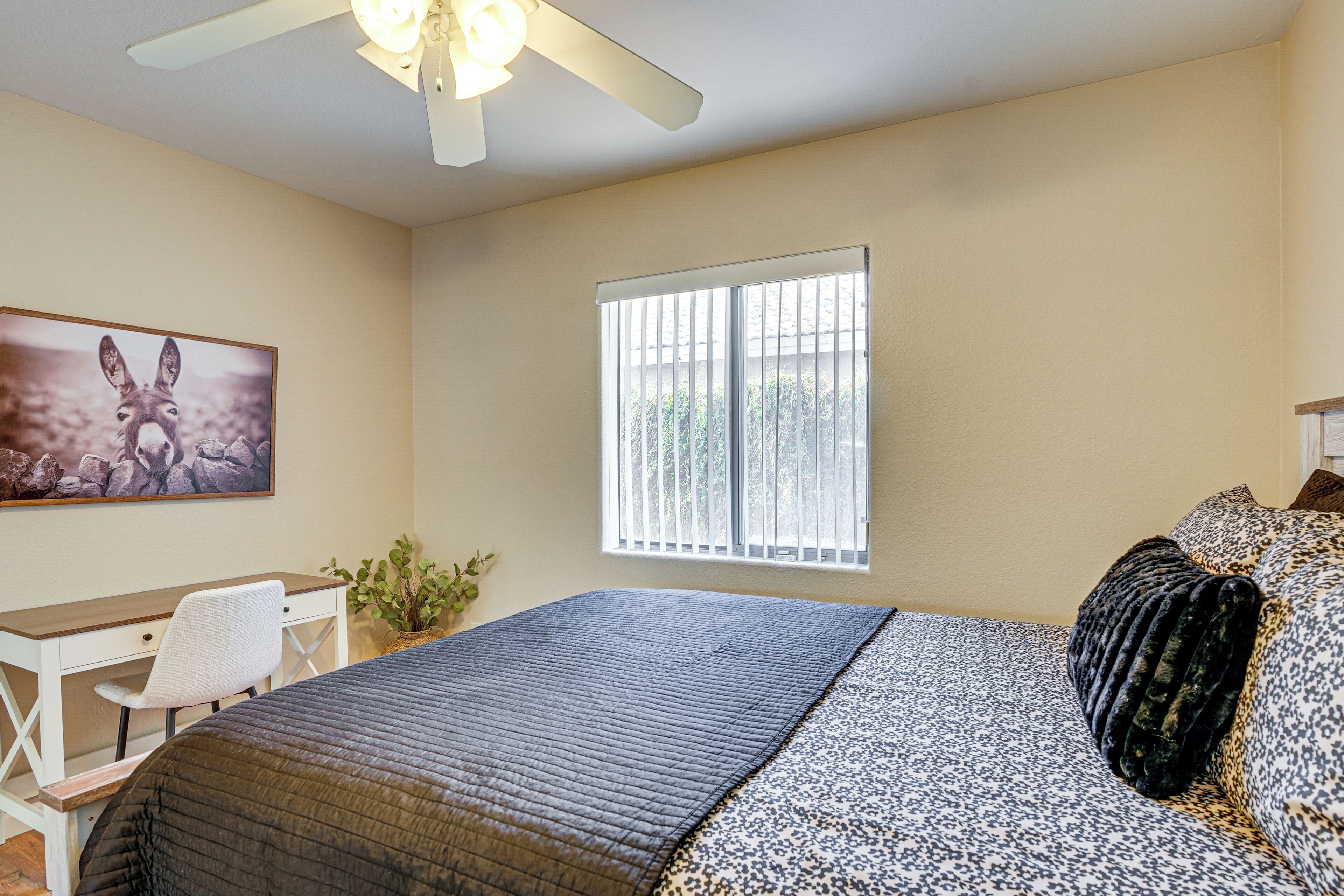 Quarto com cama, escrivaninha, cadeira, janela e ventilador de teto.