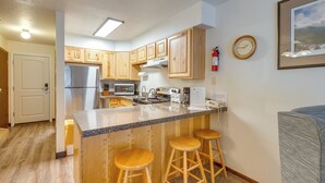 A kitchen with wooden cabinets, a stainless steel refrigerator, a microwave, a stove, and a sink. There are three wooden stools at the island. - Unwind Poolside, Walk to Main St! Winter Park Stay (Winter Park)
