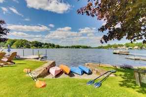 Un entorno junto al lago con kayaks y tablas de remo sobre el césped, un muelle y vistas al agua y la vegetación circundante.