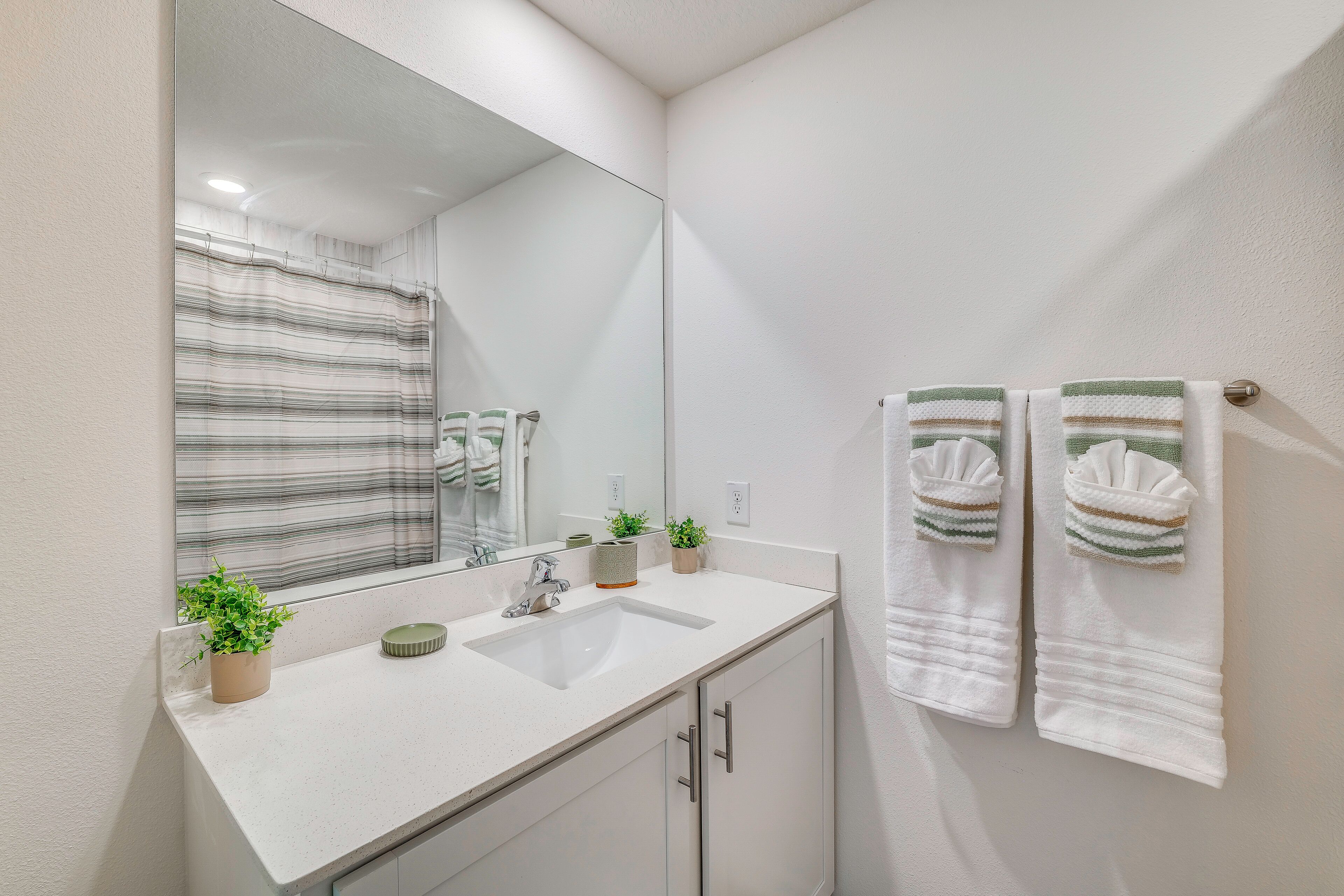 A bathroom with a white sink, a mirror, a striped shower curtain, and two towels on a rack.