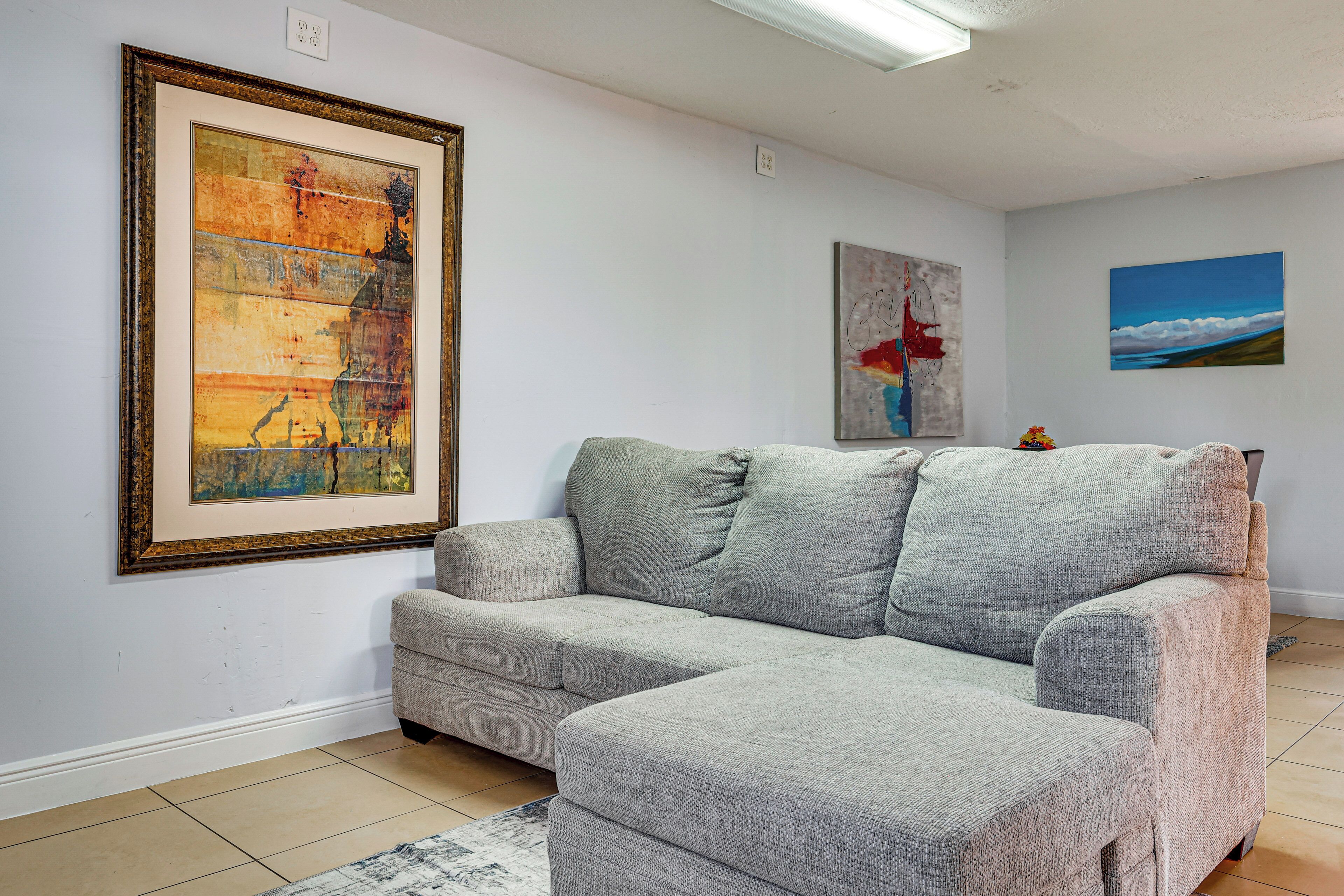 Un soggiorno con un divano modulare grigio, un quadro astratto incorniciato e un dipinto di paesaggio appeso al muro.