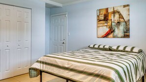 Een slaapkamer met een bed, een deur, een aan de muur hangend schilderij en een kast.
