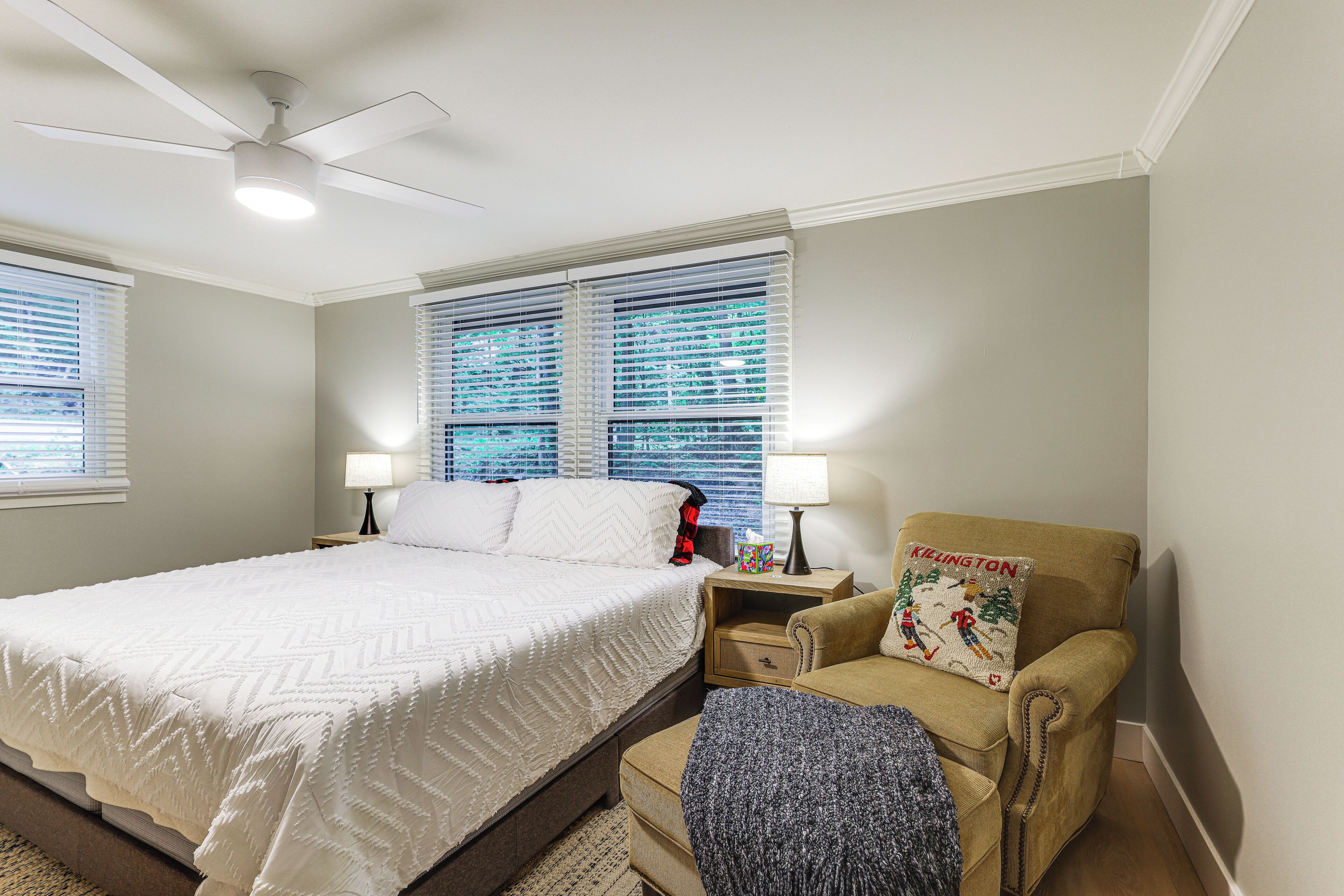A bedroom with a bed, nightstands, a chair, a ceiling fan, and a window with blinds.