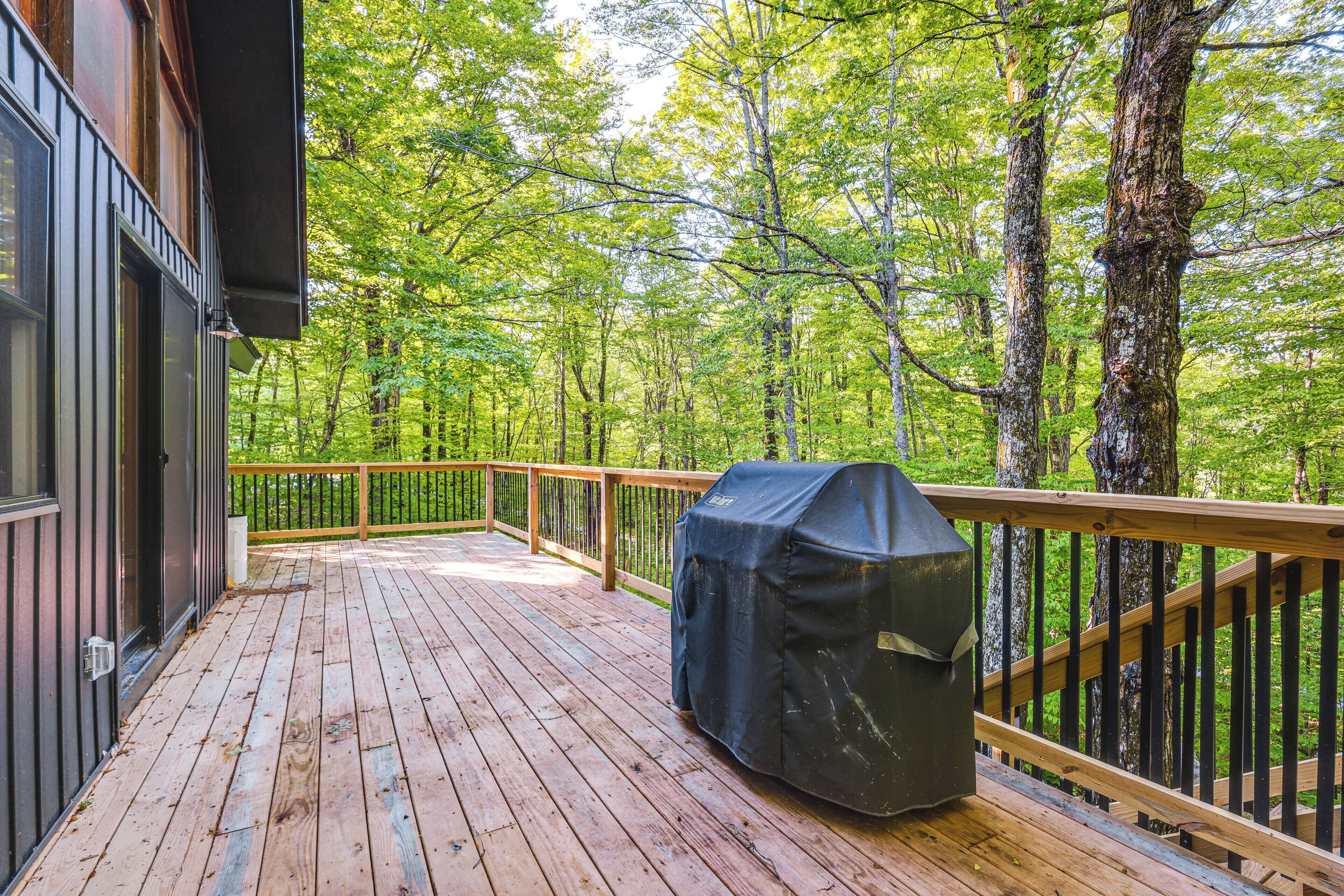 A wooden deck with a barbecue grill, surrounded by trees.