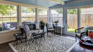 Ein Wintergarten mit Deckenventilator, großen Fenstern, einem gemusterten Teppich und Blick ins Freie.