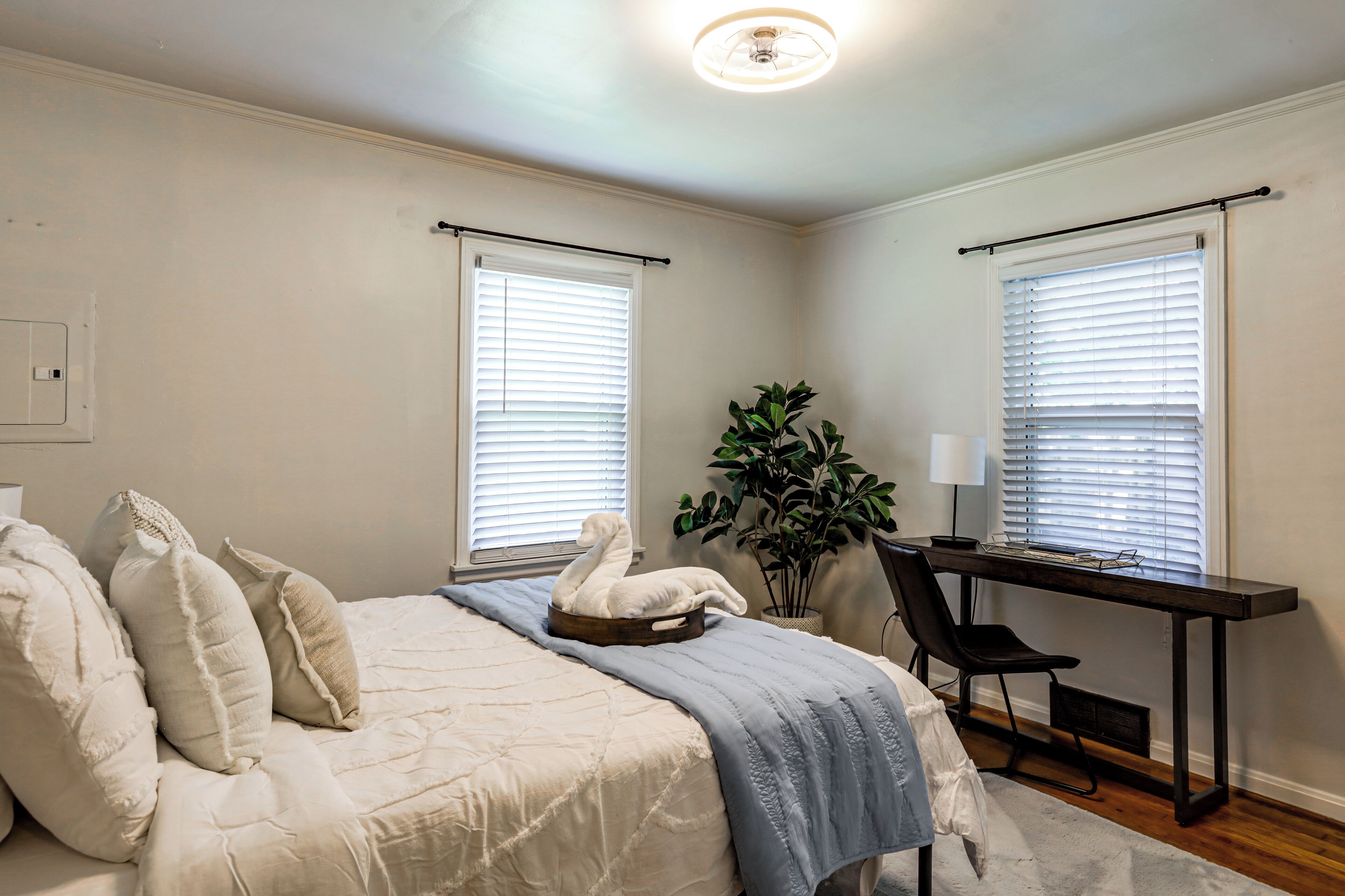 A bedroom with a bed, a desk, and two windows with blinds.