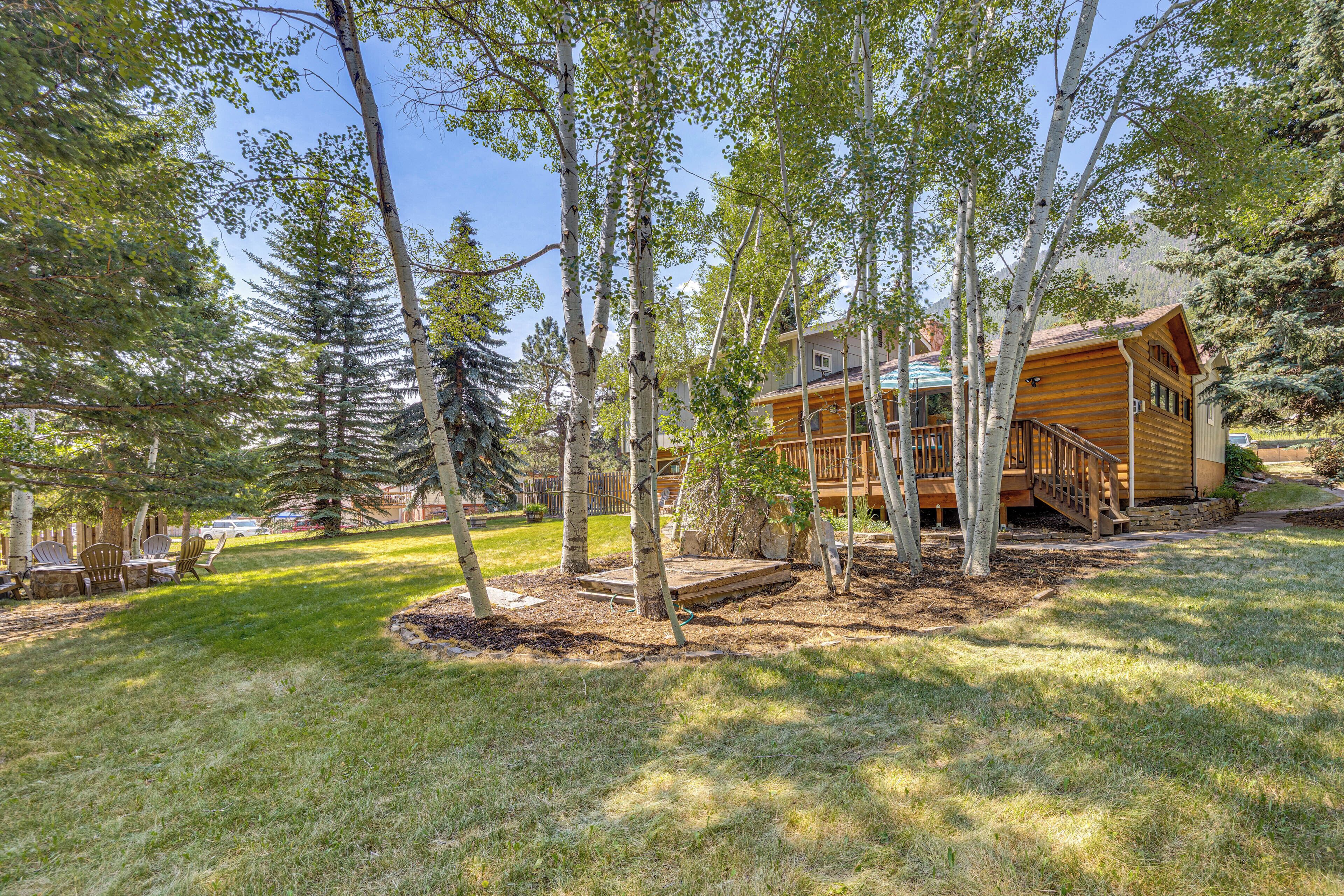 A wooden cabin with a deck, surrounded by trees and a grassy yard.