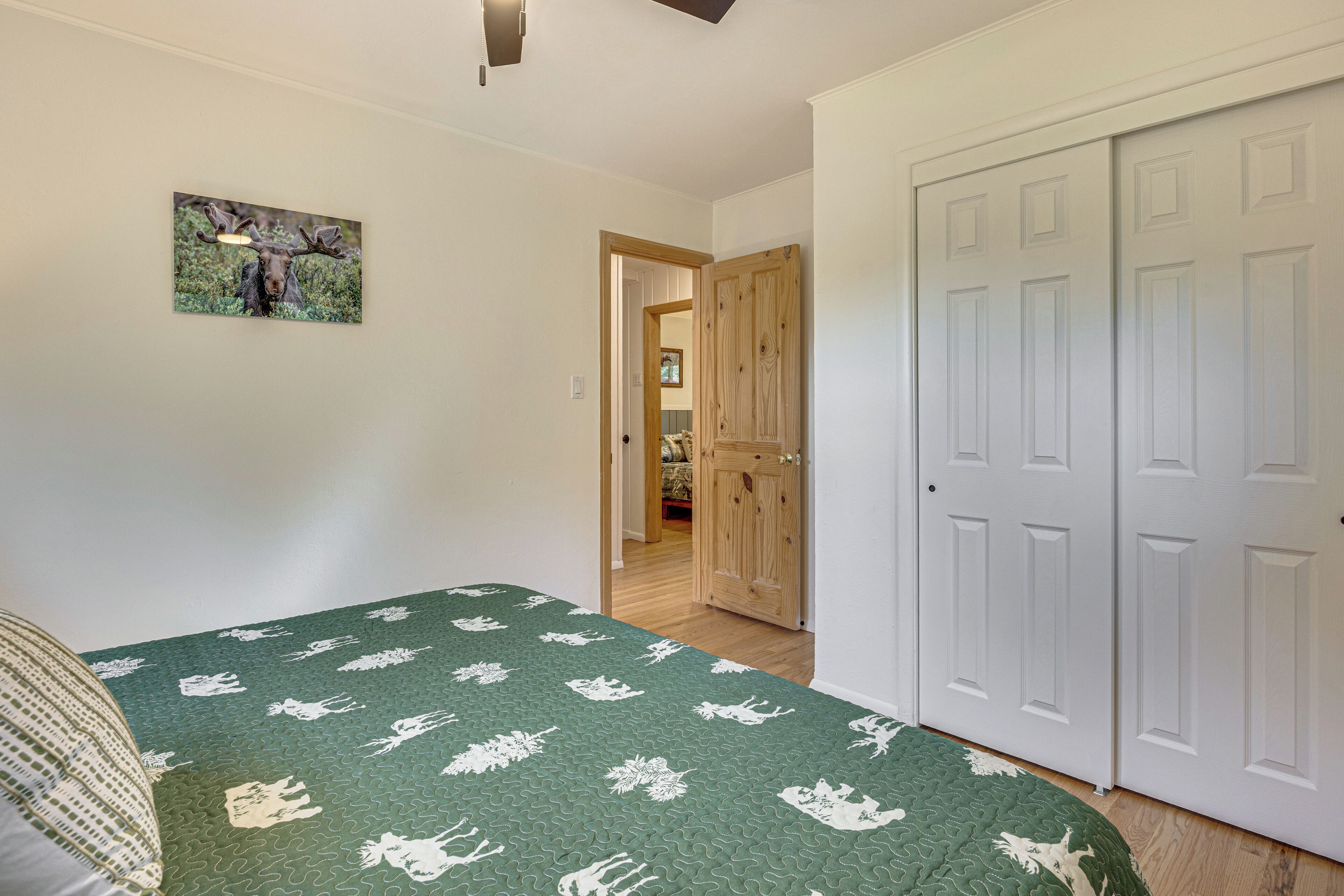 A bedroom with a green patterned bedspread, a wooden door, and a framed picture on the wall.
