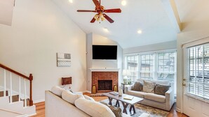 A living room with a fireplace, a ceiling fan, and a staircase.