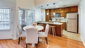 A kitchen with wooden cabinets, a stainless steel refrigerator, and a dining area with a round table and chairs.