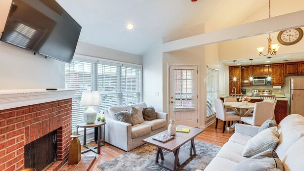 A living room with a fireplace, sofa, coffee table, and a dining area with a kitchen in the background.