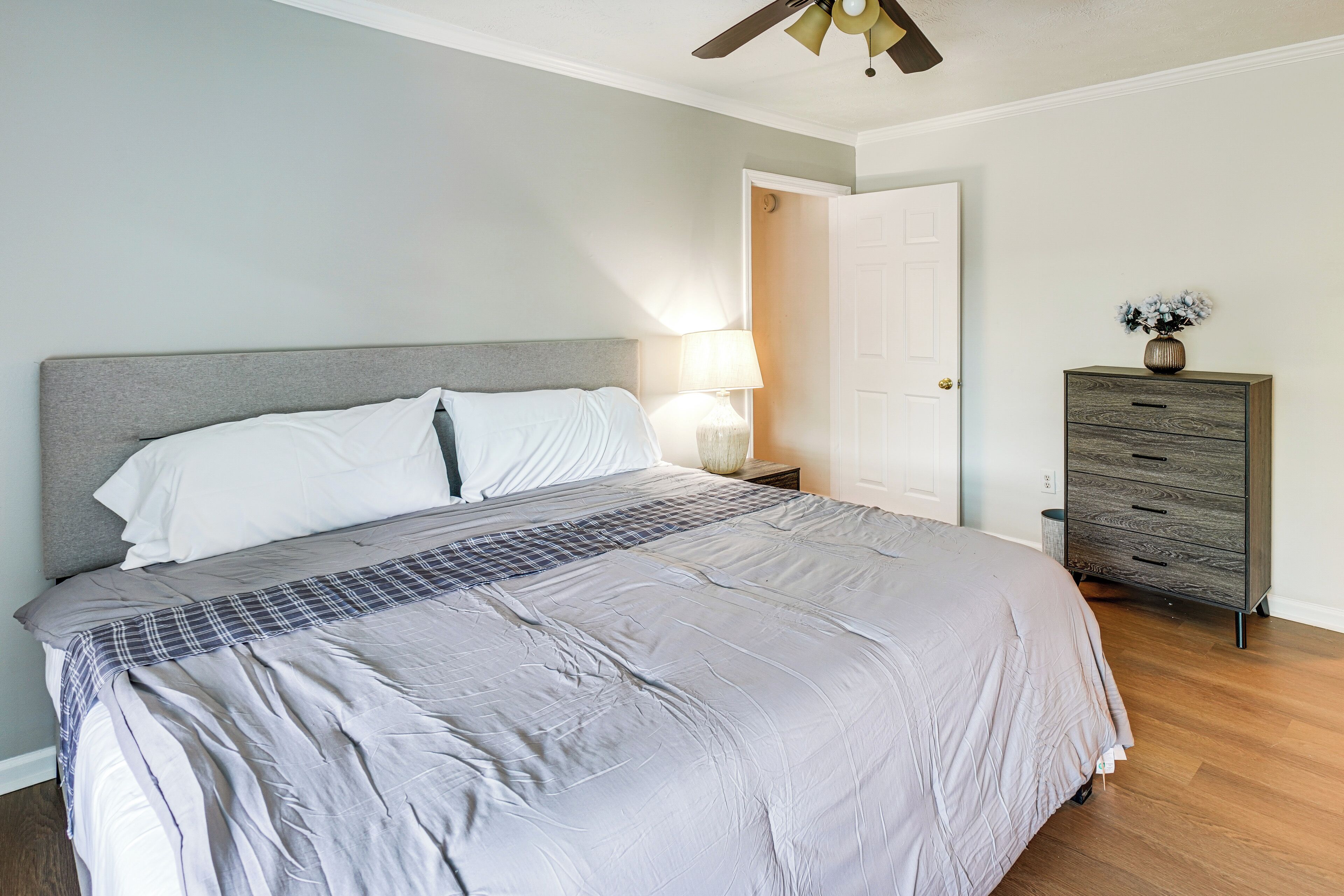 Un dormitorio con cama, lámpara de noche, cómoda y una puerta.