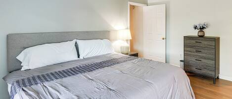 Un dormitorio con cama, lámpara de noche, cómoda y una puerta.
