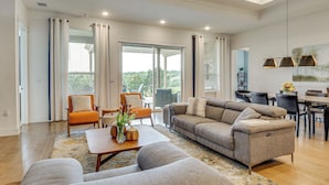 Ein geräumiges Wohnzimmer mit einer Couch, einem Couchtisch und Sesseln, ein Essbereich mit Tisch und Stühlen sowie große Fenster mit Vorhängen.