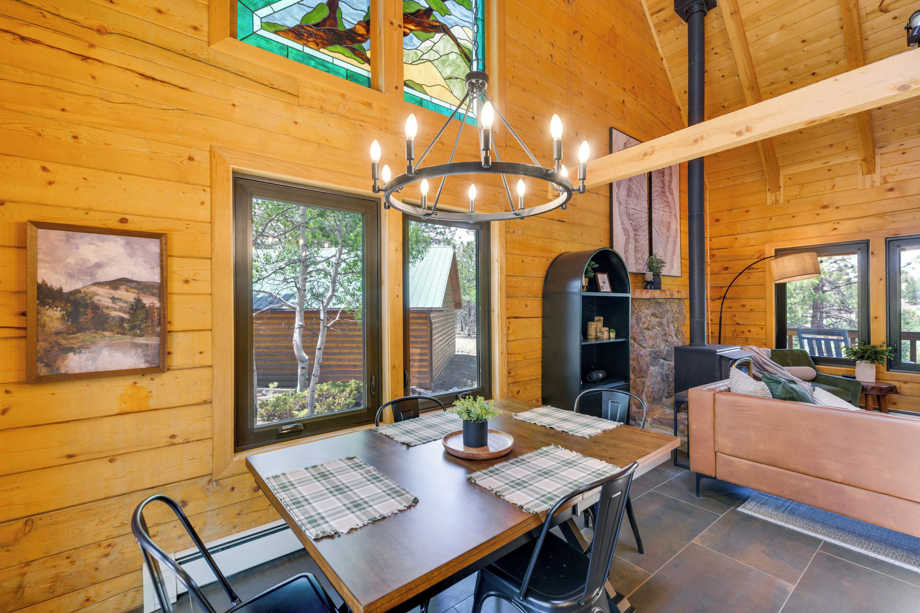 A wooden interior with a dining table, chairs, a sofa, and a chandelier.
