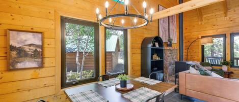 A wooden interior with a dining table, chairs, a sofa, and a chandelier.