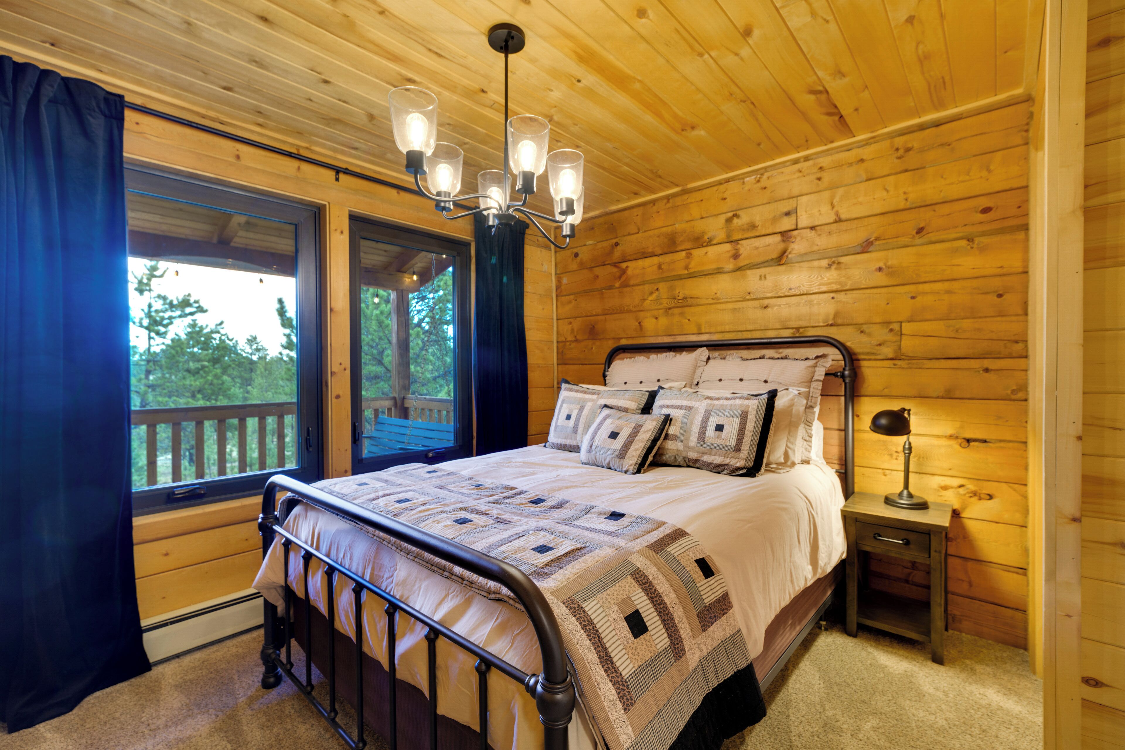 A wooden cabin bedroom with a bed, a nightstand, a lamp, and a window with curtains.