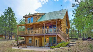 Eine zweistöckige Blockhütte mit Balkon, überdachter Terrasse und Picknicktisch.