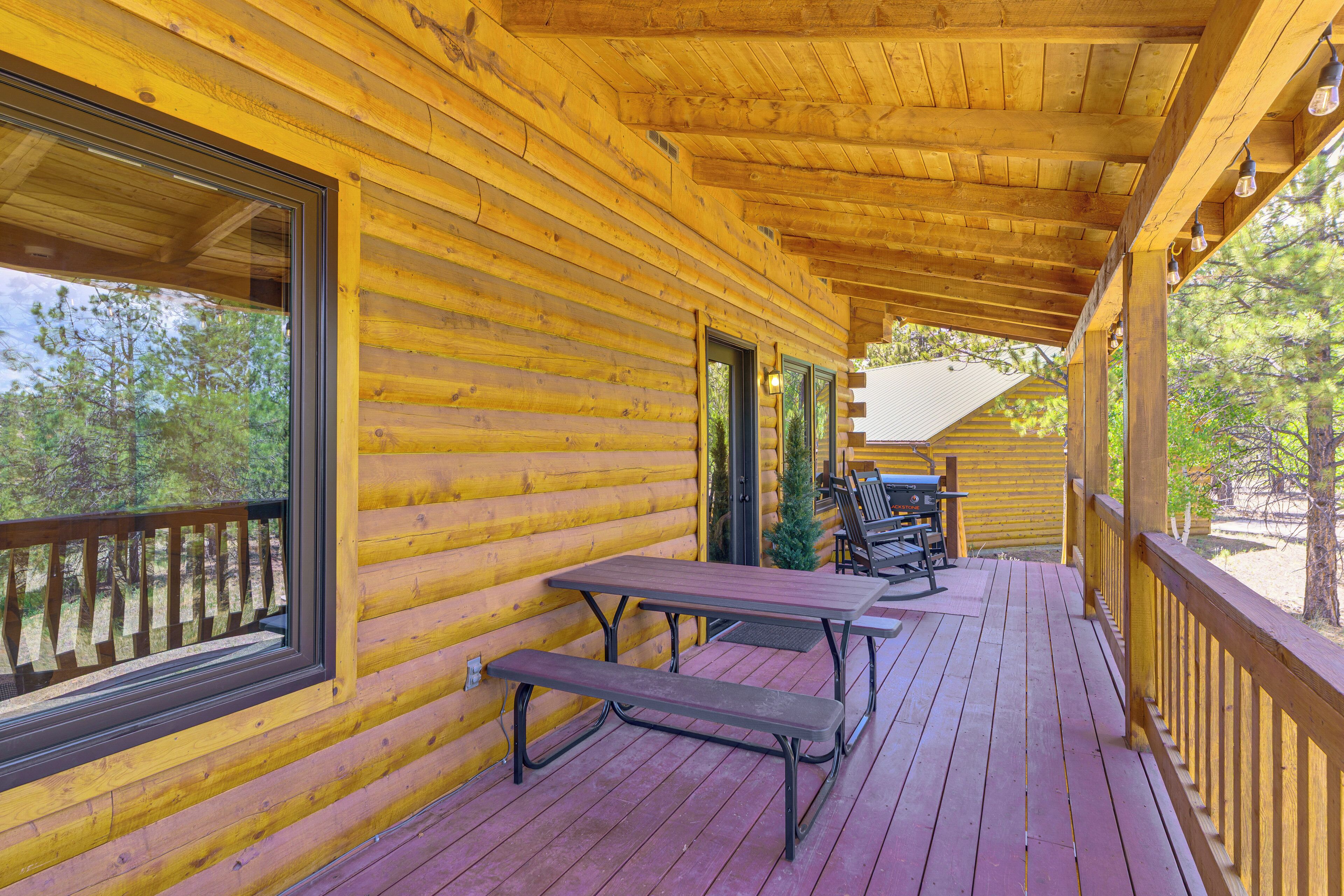 A wooden cabin with a covered porch, a picnic table, and a view of trees.