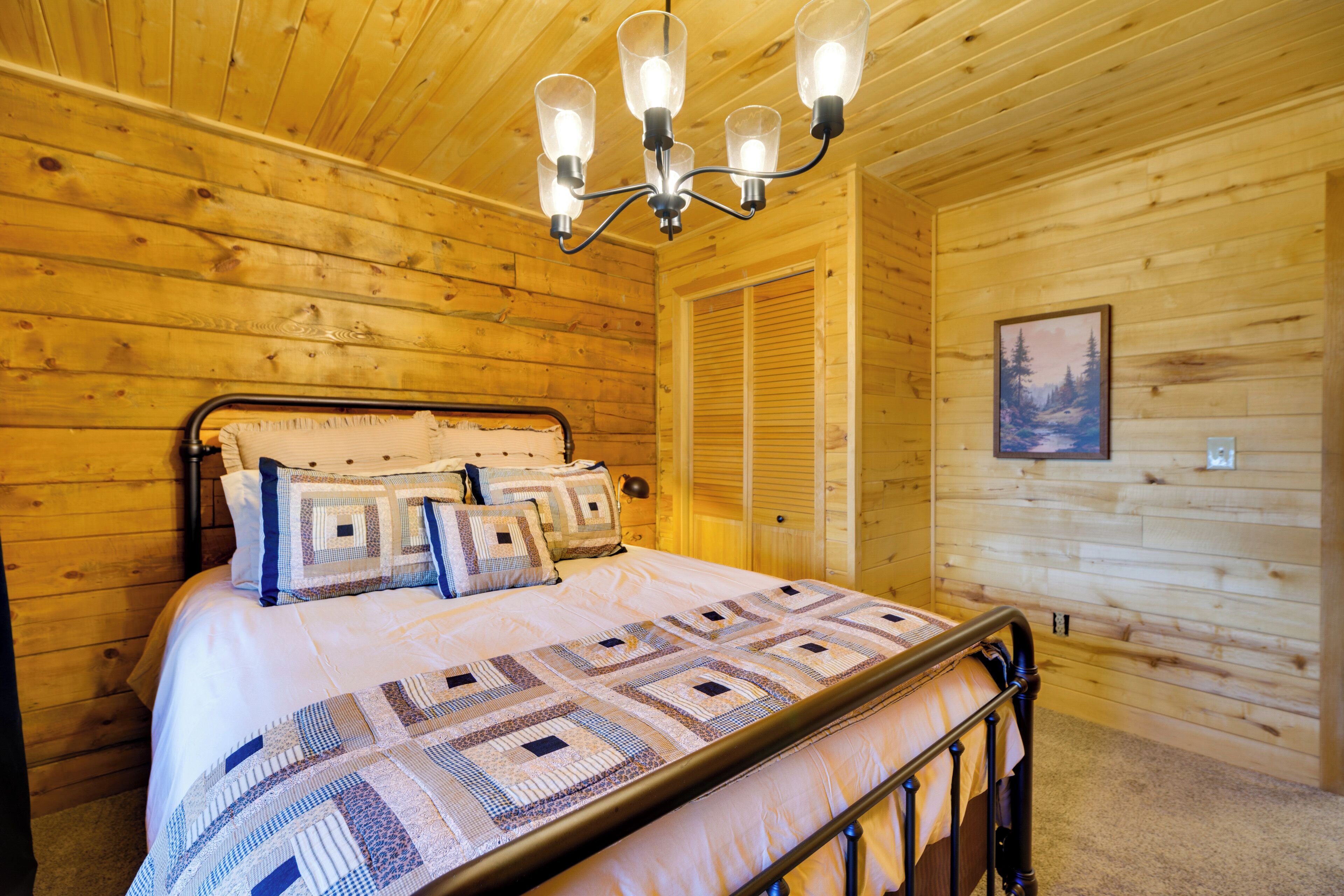 A wooden cabin bedroom with a bed, a chandelier, and a painting on the wall.
