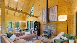 Ein gemütliches Blockhauss-Interieur mit Ledersofa, Kamin aus Stein und Essbereich.