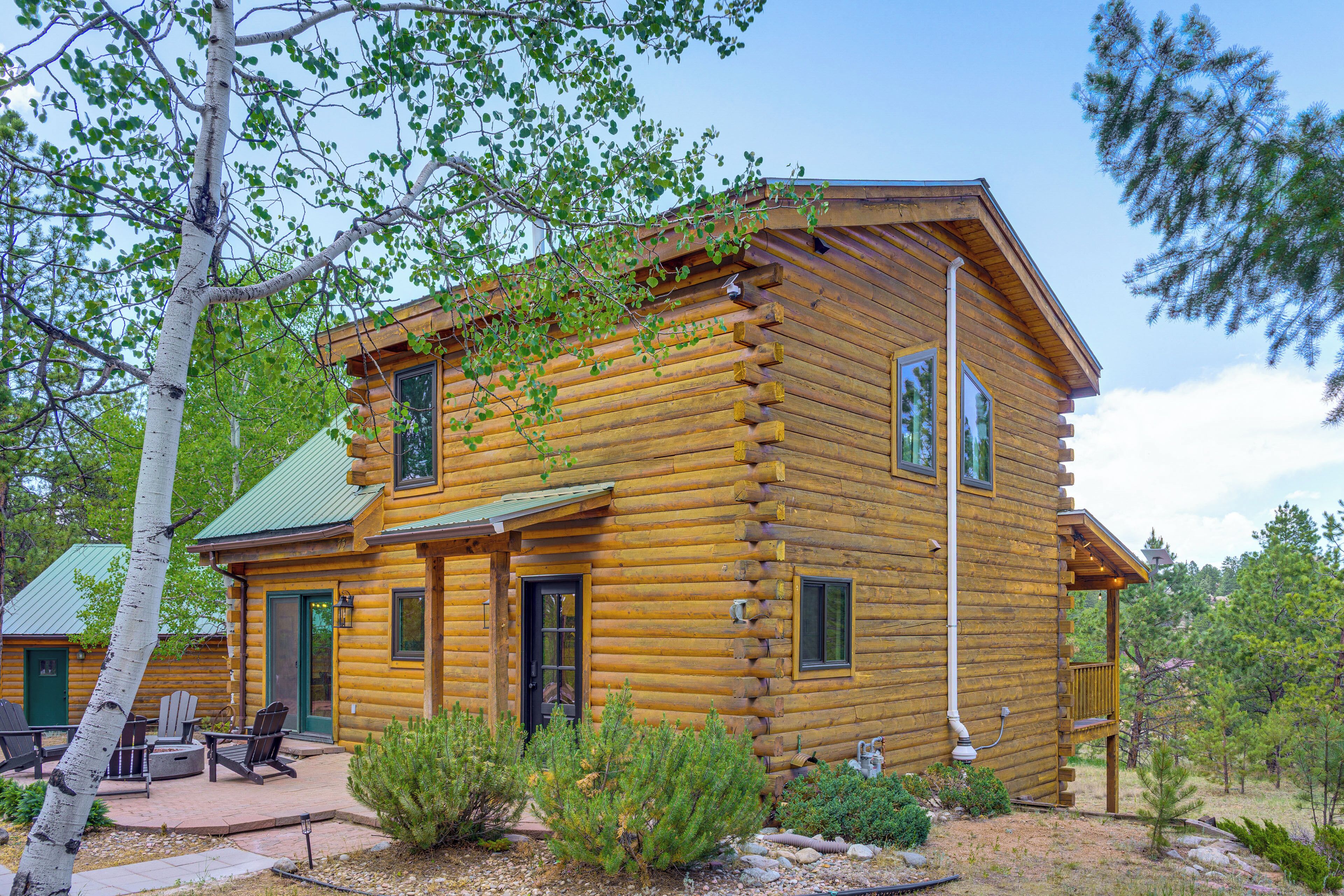 A log cabin with a porch, outdoor seating, and a view of the surrounding forest.