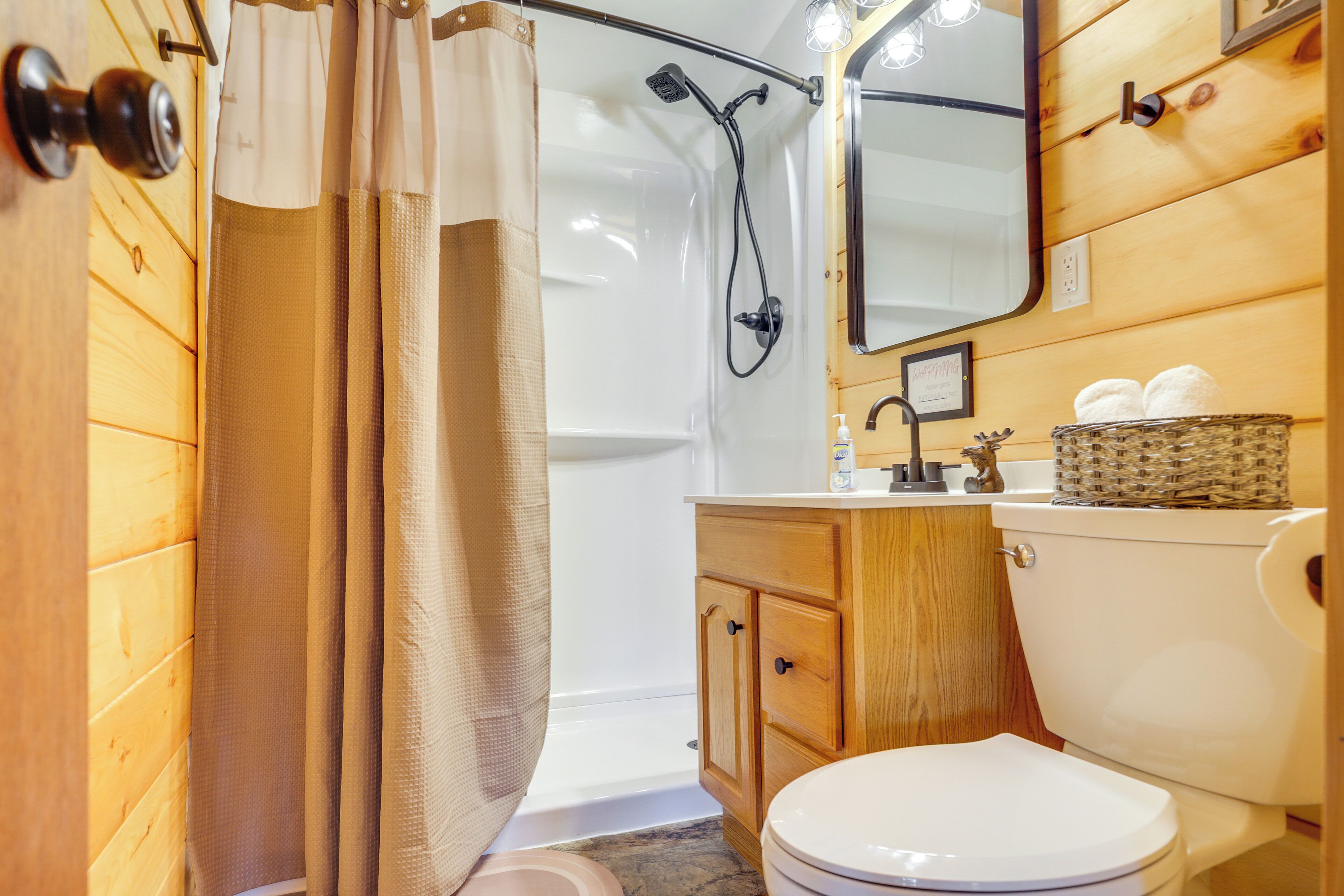 A wooden-paneled bathroom with a shower, toilet, vanity, and mirror.