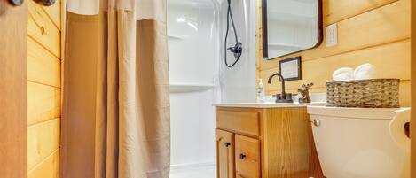 Baño con paneles de madera, ducha, inodoro, tocador y espejo.
