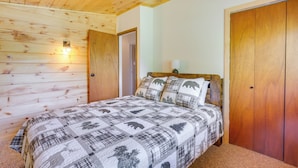 Ein Schlafzimmer mit Holzbalkendecke, einem Bett mit gemustertem Quilt, einem Nachttisch mit Lampe und einem Holzschrank.