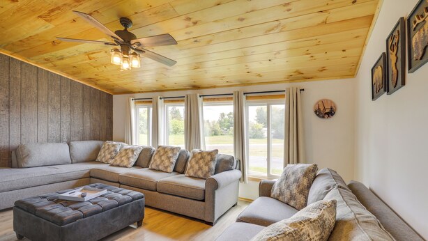 Ein modernes Wohnzimmer mit Ecksofa, Hocker, Deckenventilator und großen Fenstern.