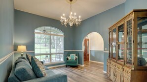 A room with a sofa, a chandelier, a cabinet, and large windows.