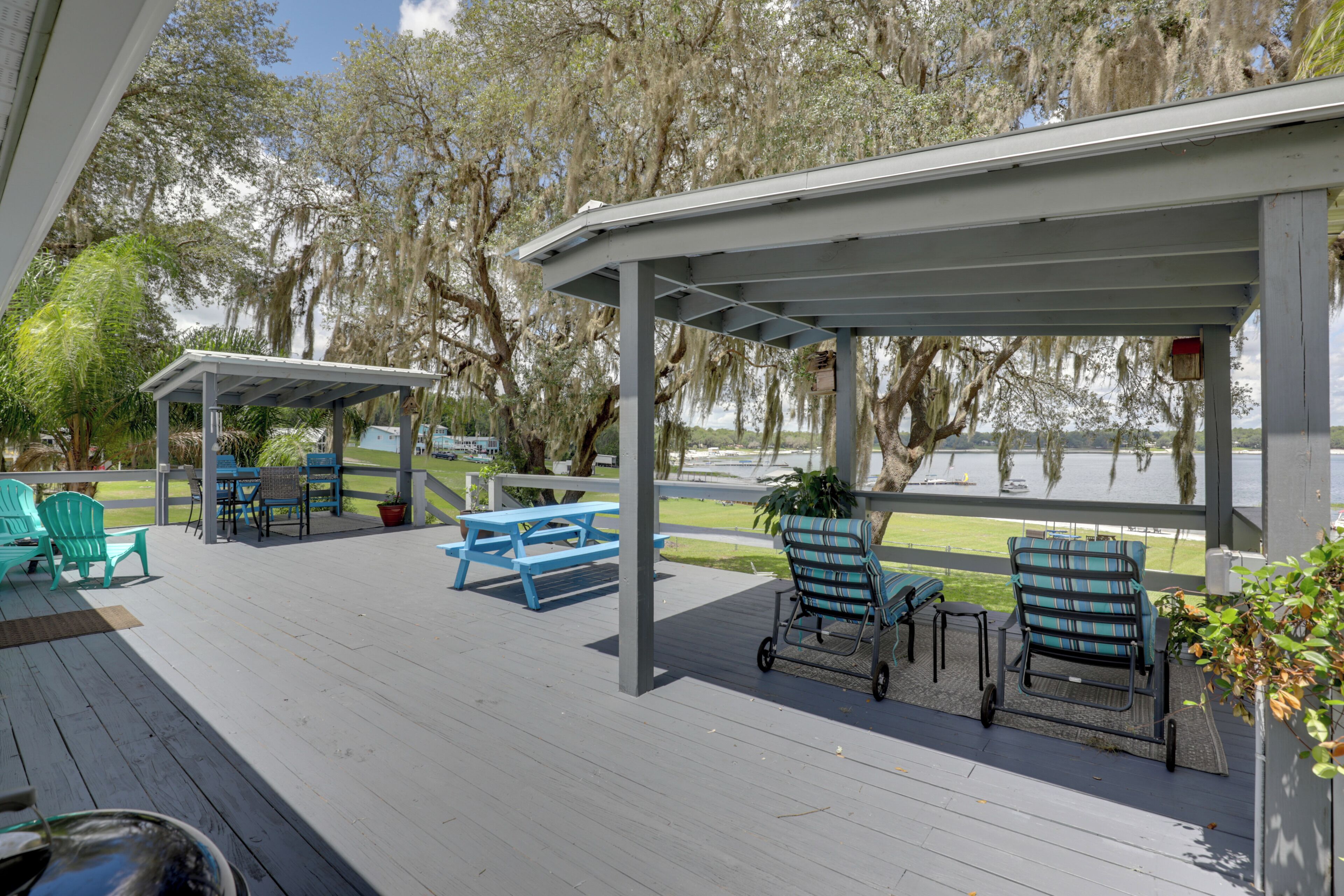 Un patio techado al aire libre con mobiliario, una mesa y vista a un cuerpo de agua.