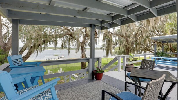 A covered outdoor seating area with chairs and tables, overlooking a body of water and trees.