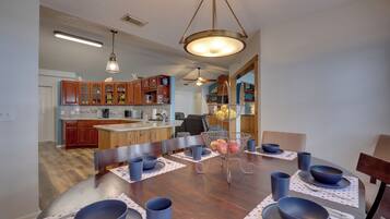A dining area with a wooden table set for four, surrounded by chairs, with a kitchen in the background.