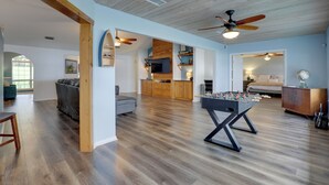 A spacious living area with a foosball table, wooden flooring, and a ceiling fan.