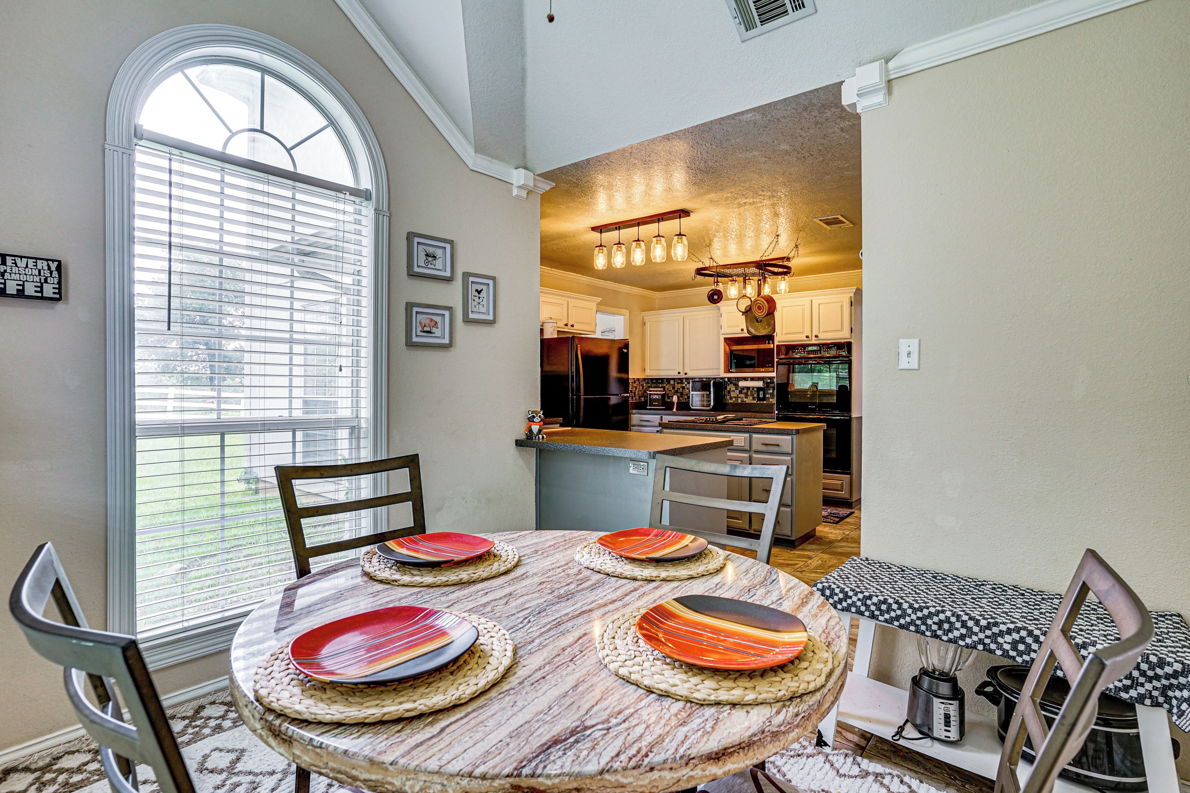 A dining area with a round table, chairs, and a view into a kitchen with modern appliances.