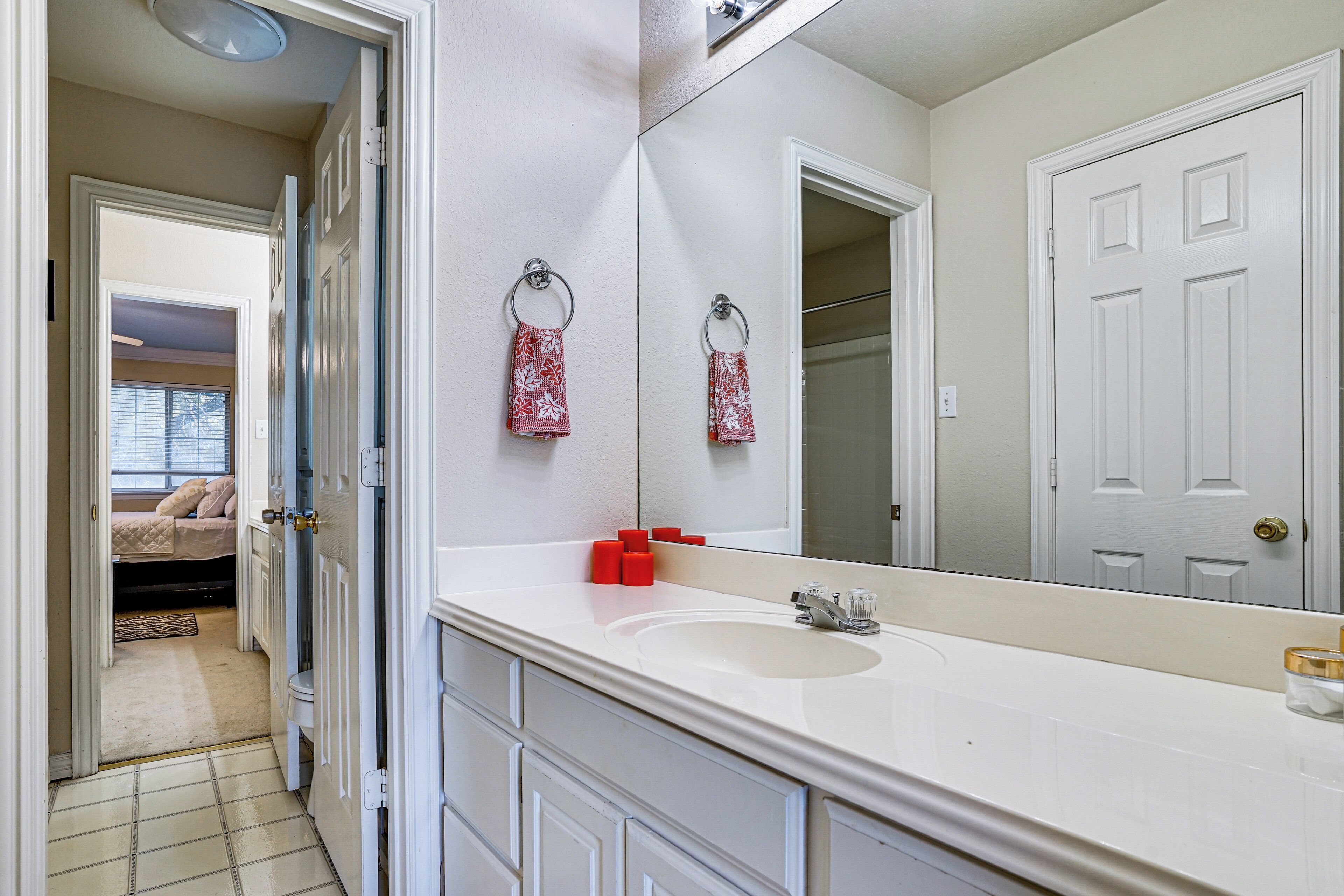 A bathroom with a white sink, a large mirror, and a door leading to a bedroom.
